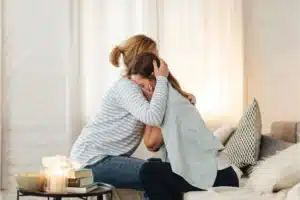 Woman comforting a crying loved one with a supportive hug ata substance abuse clinic.