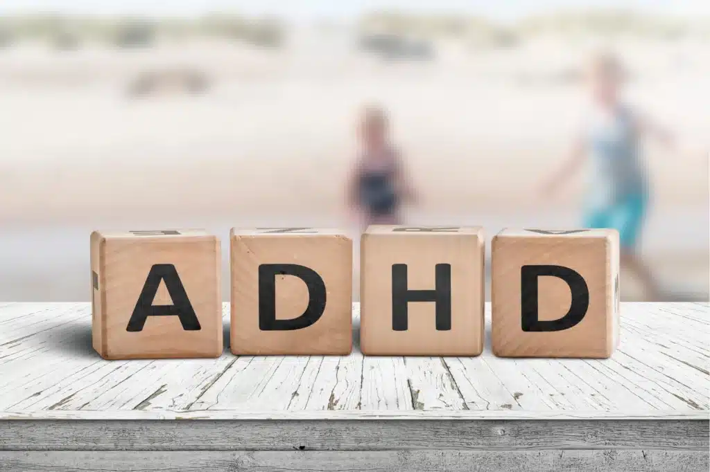Wooden blocks spelling ADHD on a table with children playing in the background.