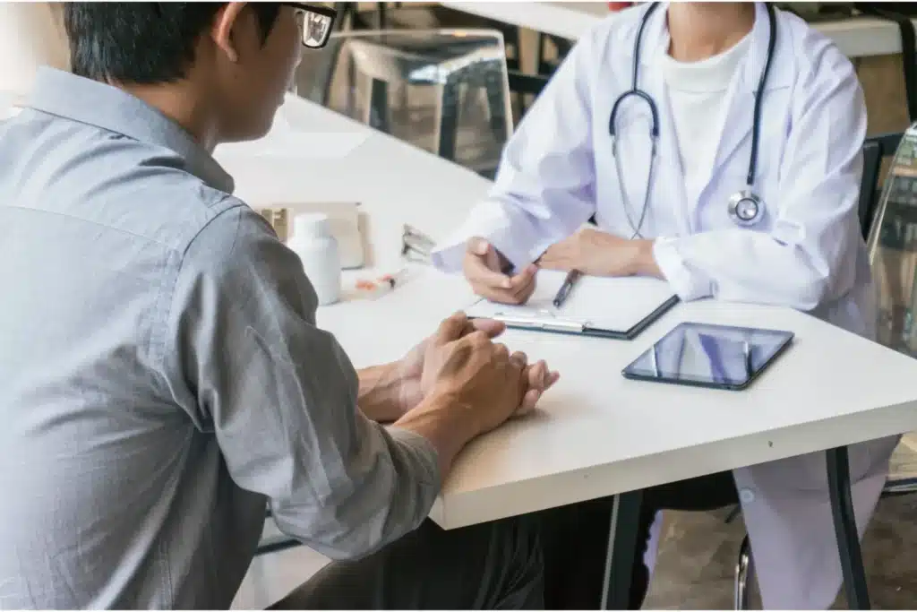 Medical appointment showing a patient and doctor talking across a desk with notes and a tablet